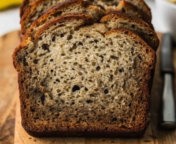 Sliced old fashioned banana bread on a wooden board with bananas