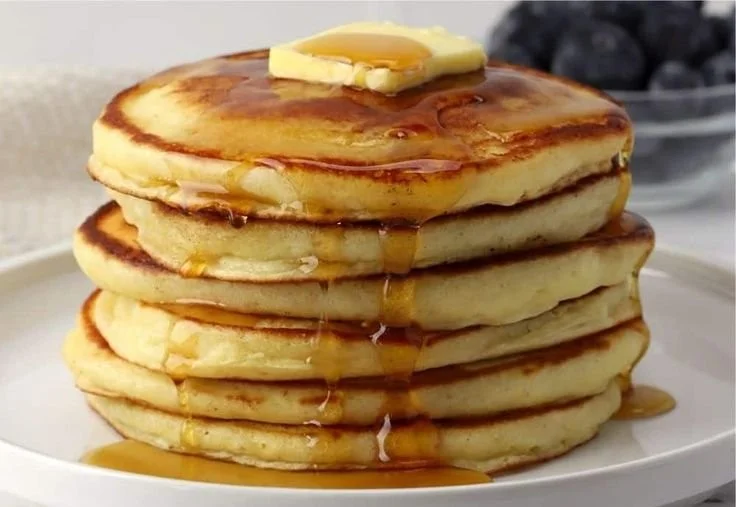 Stack of fluffy classic pancakes served with syrup and berries
